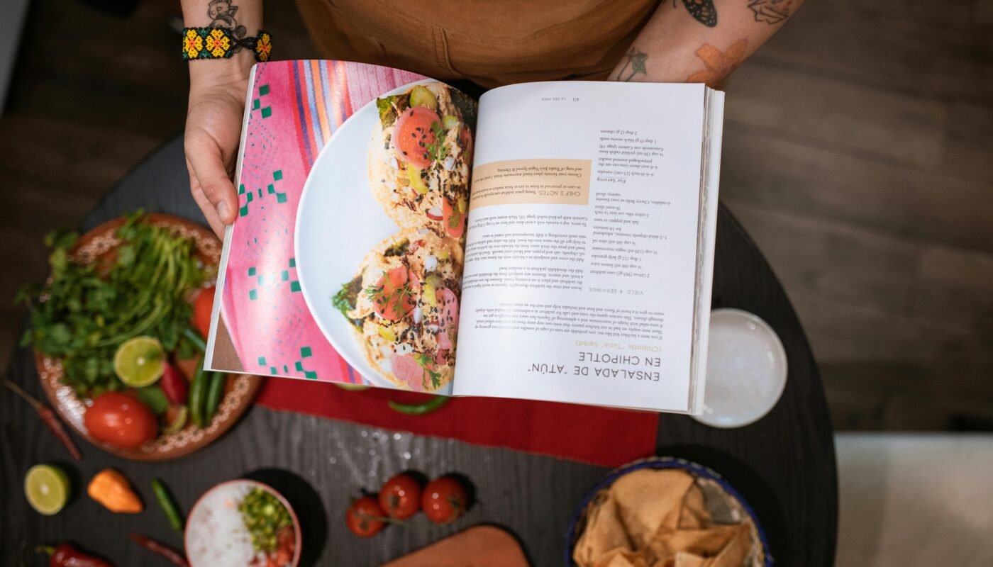 Close-up of chef holding cookbook over Mexican ingredients on table.